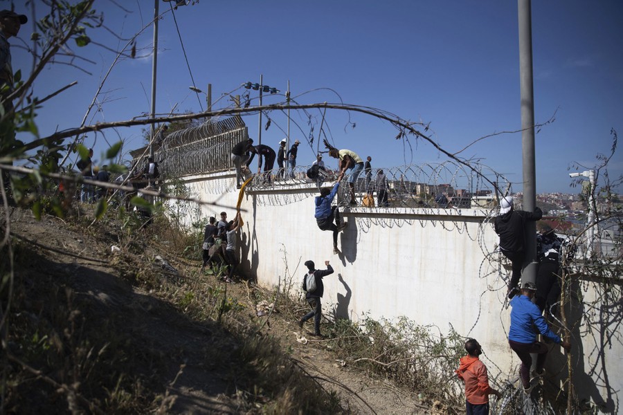 Several people scale a tall fence.