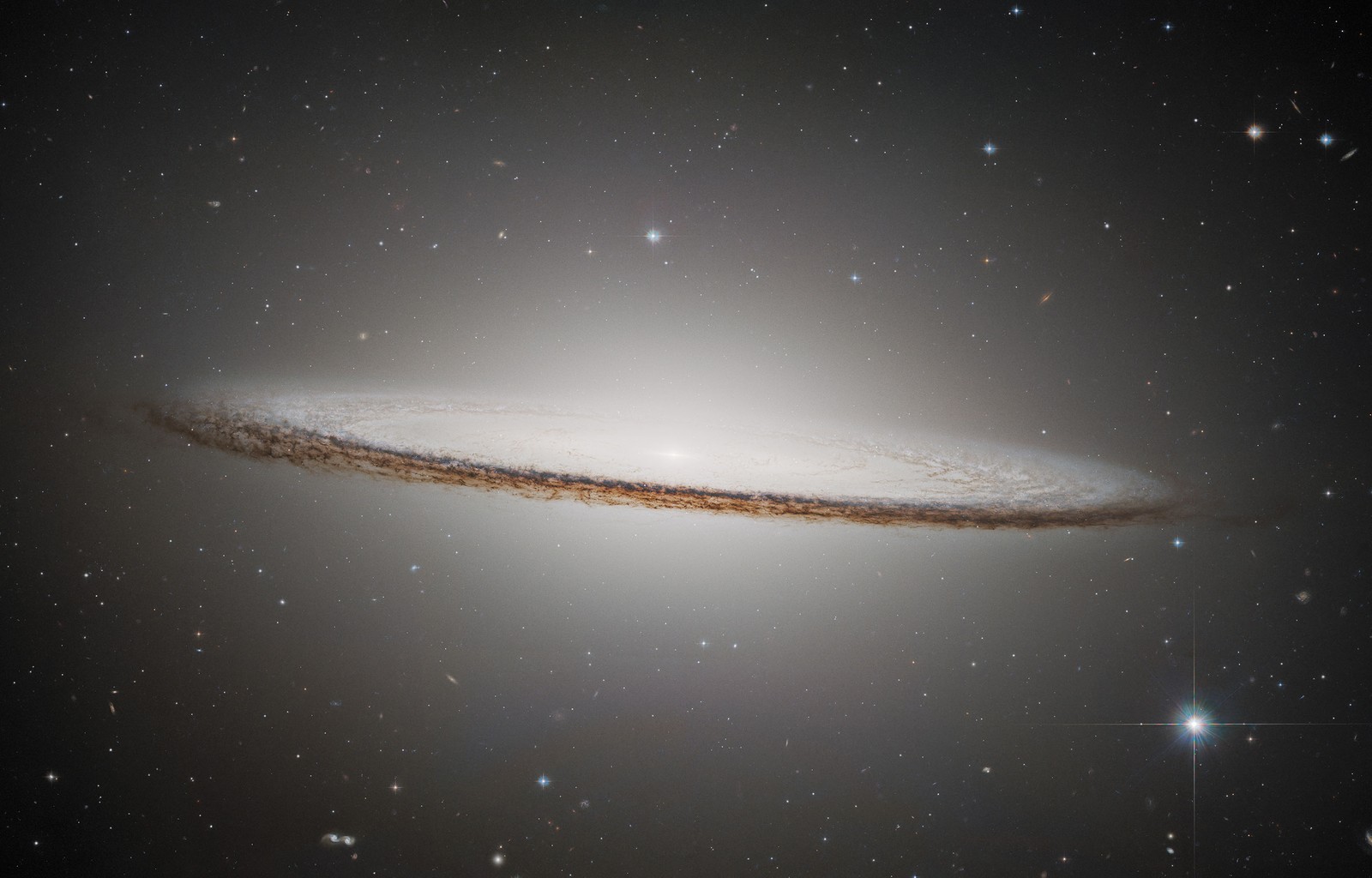 A bright, elliptical galaxy, seen edge-on, with a distinct dark lane of dust across its center