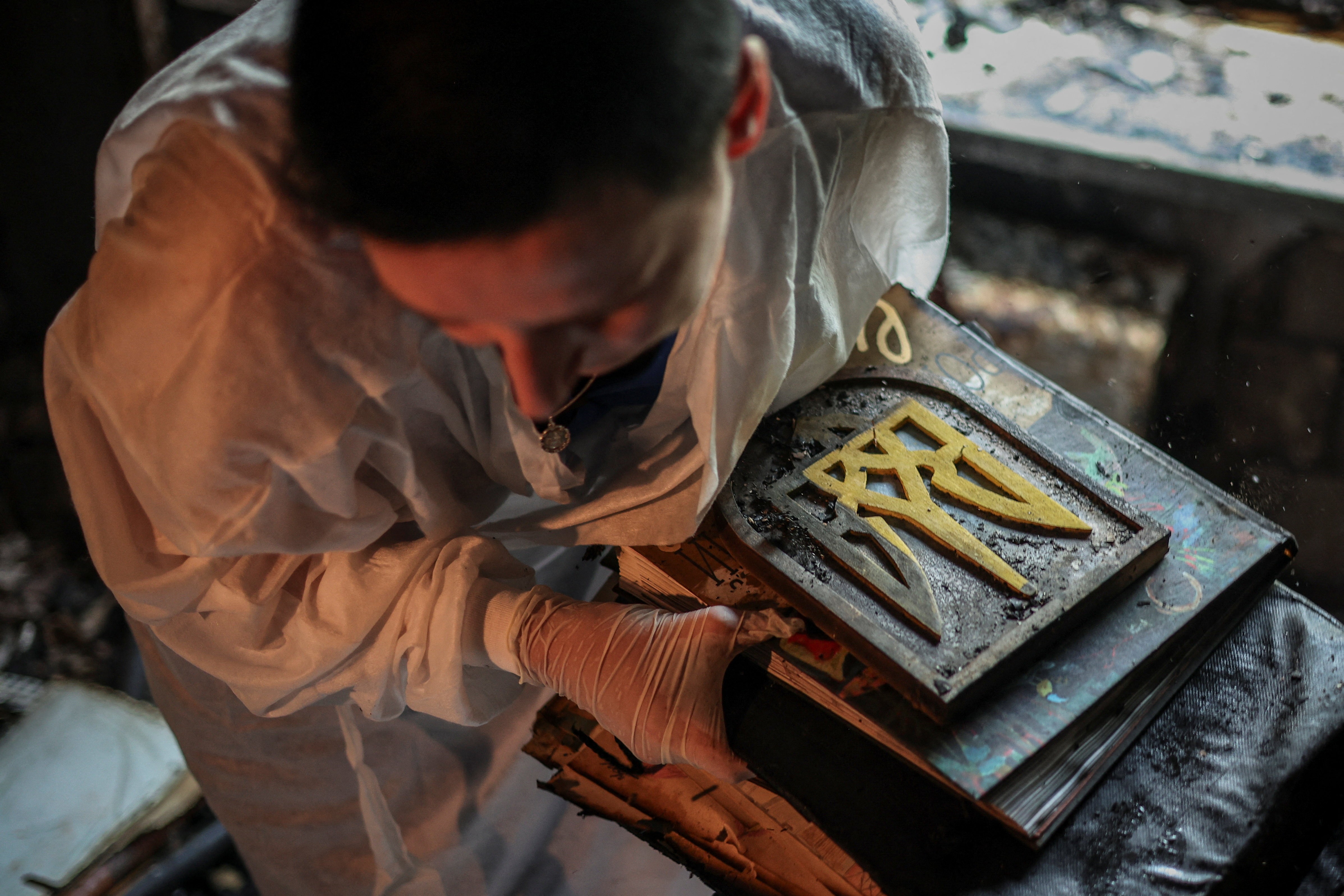 A person carries damaged books, albums, and a wooden coat of arms from a burned apartment.
