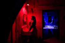 Two people are seen in separate rooms, one lit by a blue light, the other by a red light.