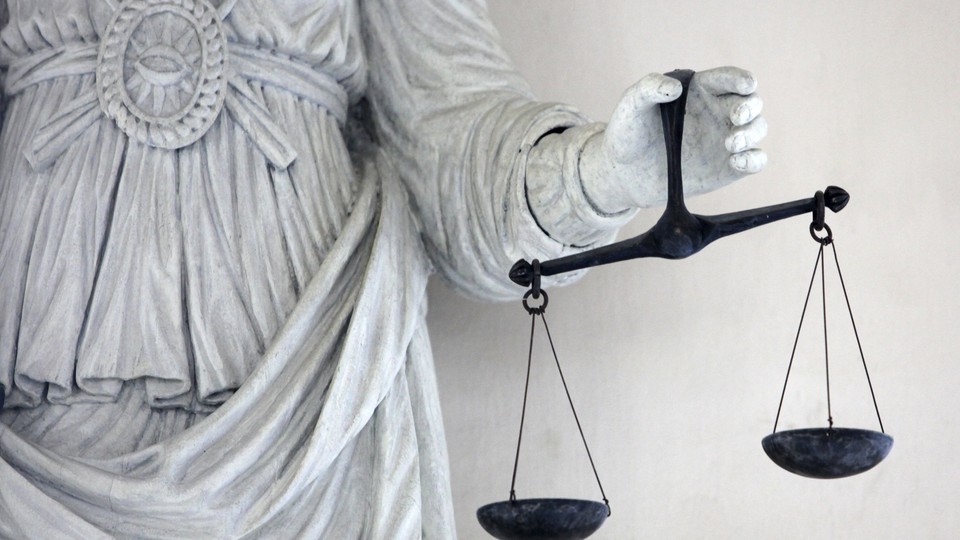 The hand of a stone statue holds a black scale of justice. 