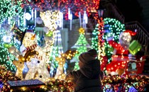 A child leans on a railing looking at illuminated Christmas decorations in front of a house.