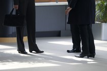 Three people in dark pants and shoes standing next to a plant