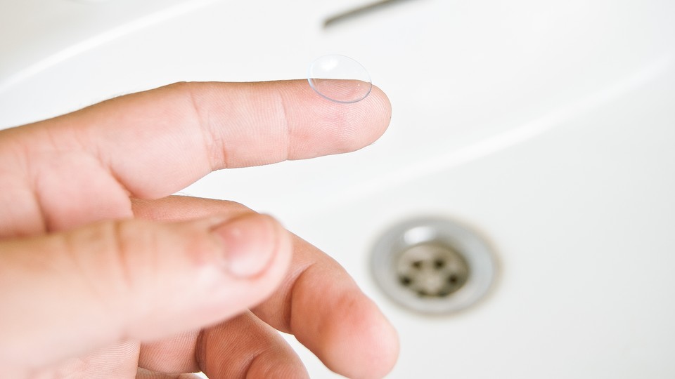 A finger holds a contact lense over a sink.