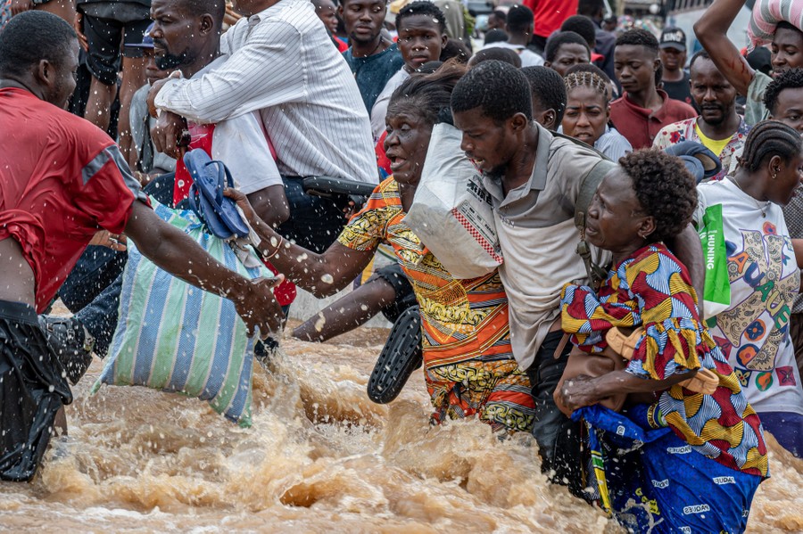 People struggle to carry belongings through fast-moving floodwater.