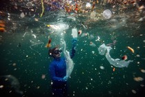 A diver floats just below the surface, surrounded by pieces of debris and plastic garbage.