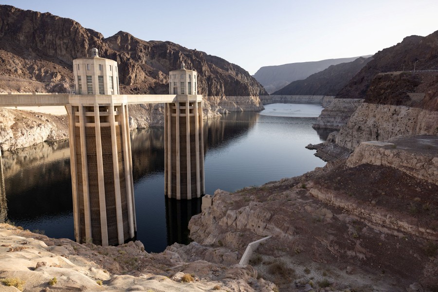 A view of a partially empty reservoir and dam structures, surrounded by rocky hills and cliffs.