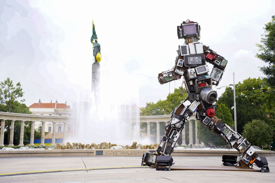 A six-meter-tall sculpture made of electronic waste, shaped like a person, stands alongside a monument.