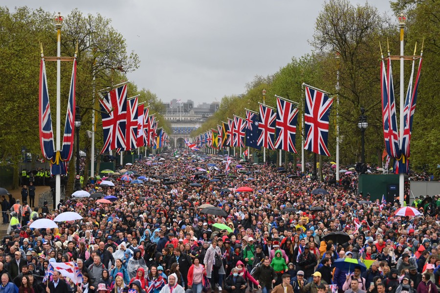 A large crowd of spectators is seen on a wide road lined with flags of the United Kingdom.