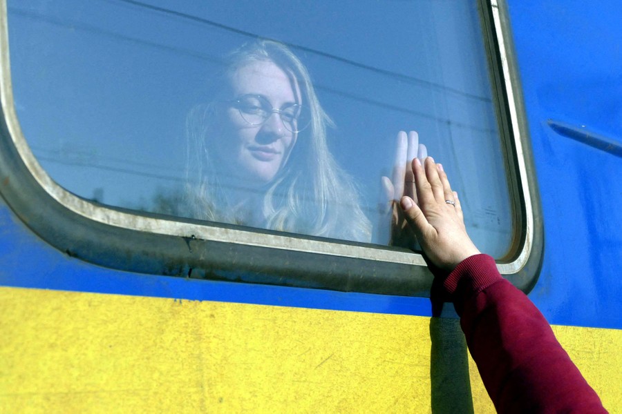 A person is seen in train window. They hold their hand to the glass, as another hand reaches up to it from outside.