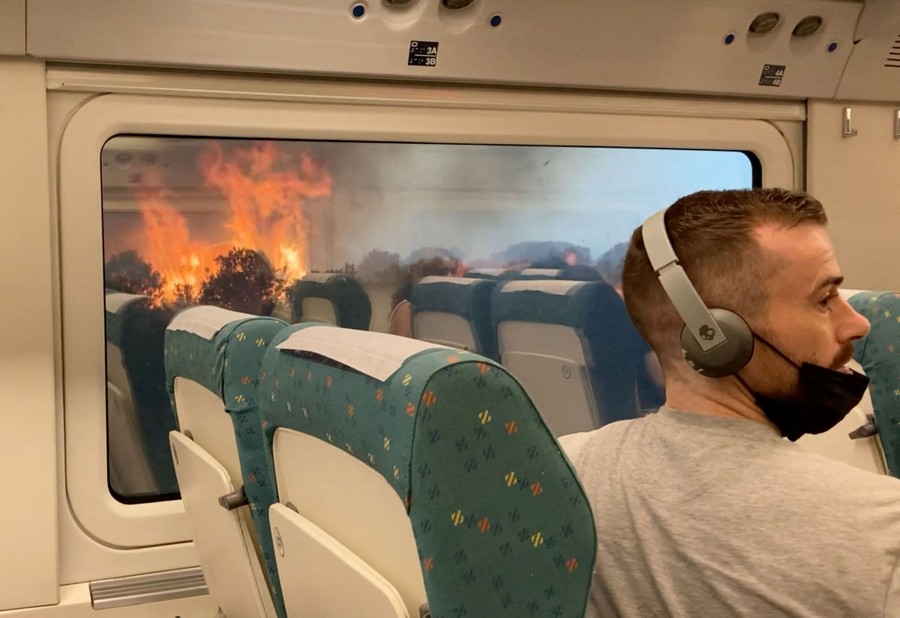 Passengers look at a wildfire from inside a train.