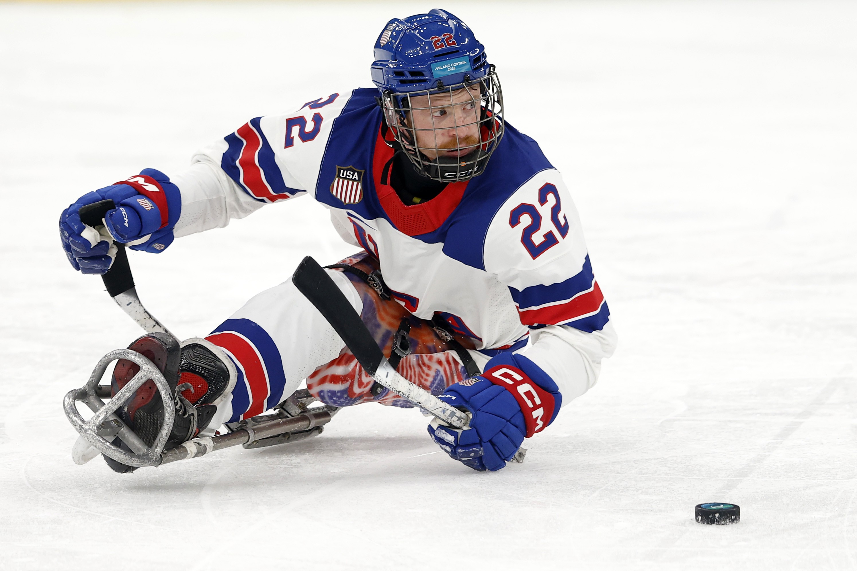 A hockey player, seated in an ice hockey sled, maneuvers with a puck during a game.