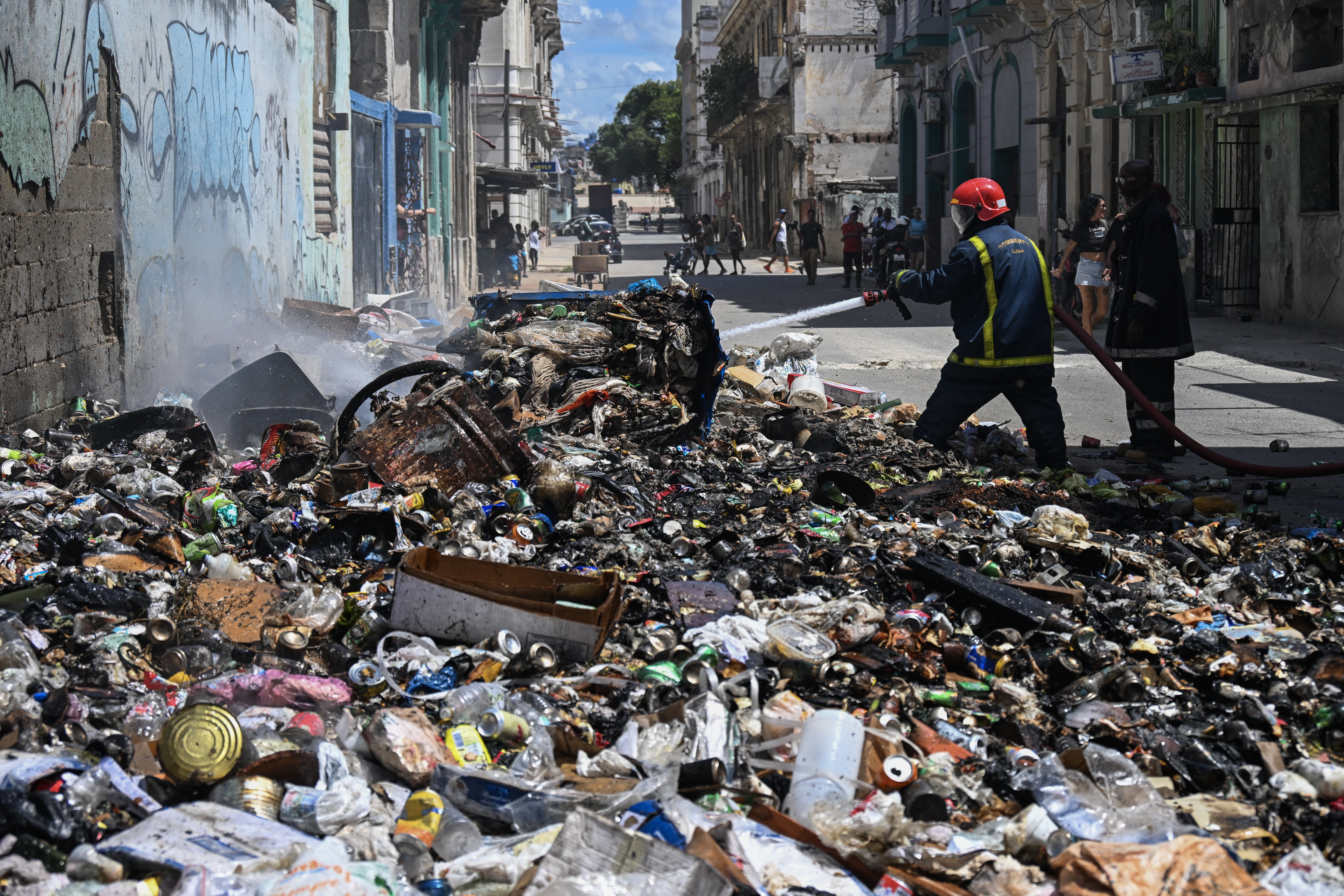 Firefighters work to put out a fire in a large pile of garbage in a street.
