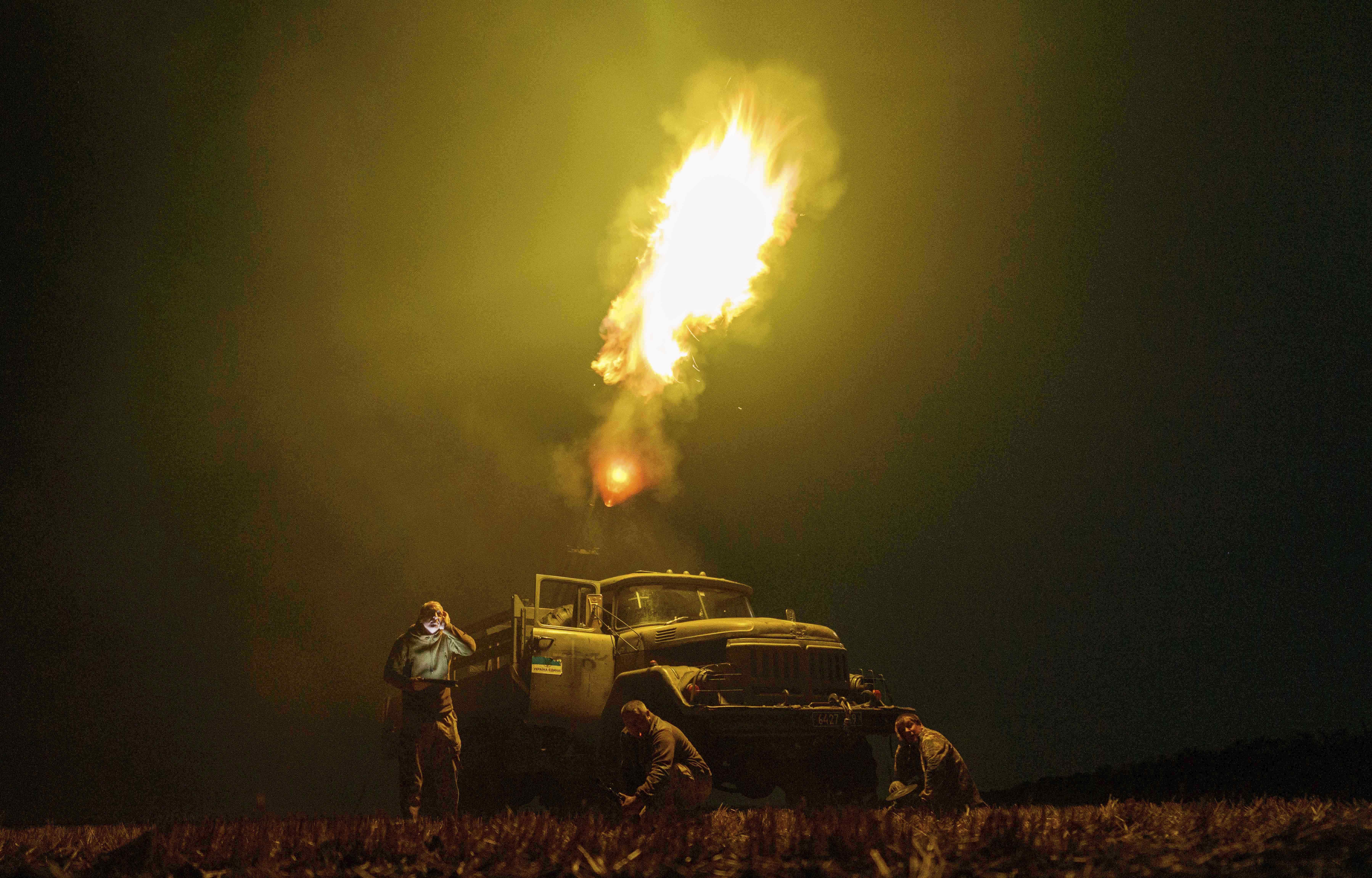 Several soldiers stand and crouch beside a truck, firing an anti-aircraft weapon.