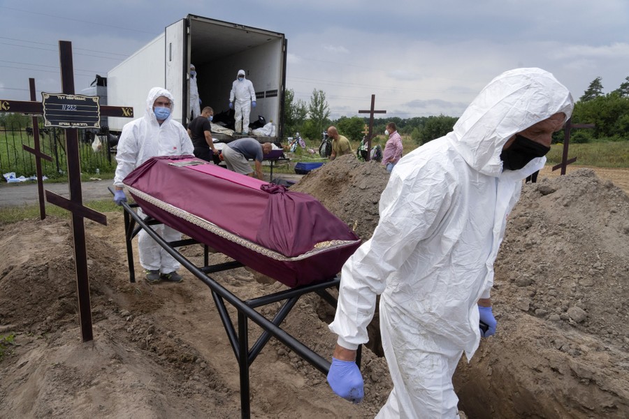 Workers wearing protective gear carry coffins from a truck into a cemetery.