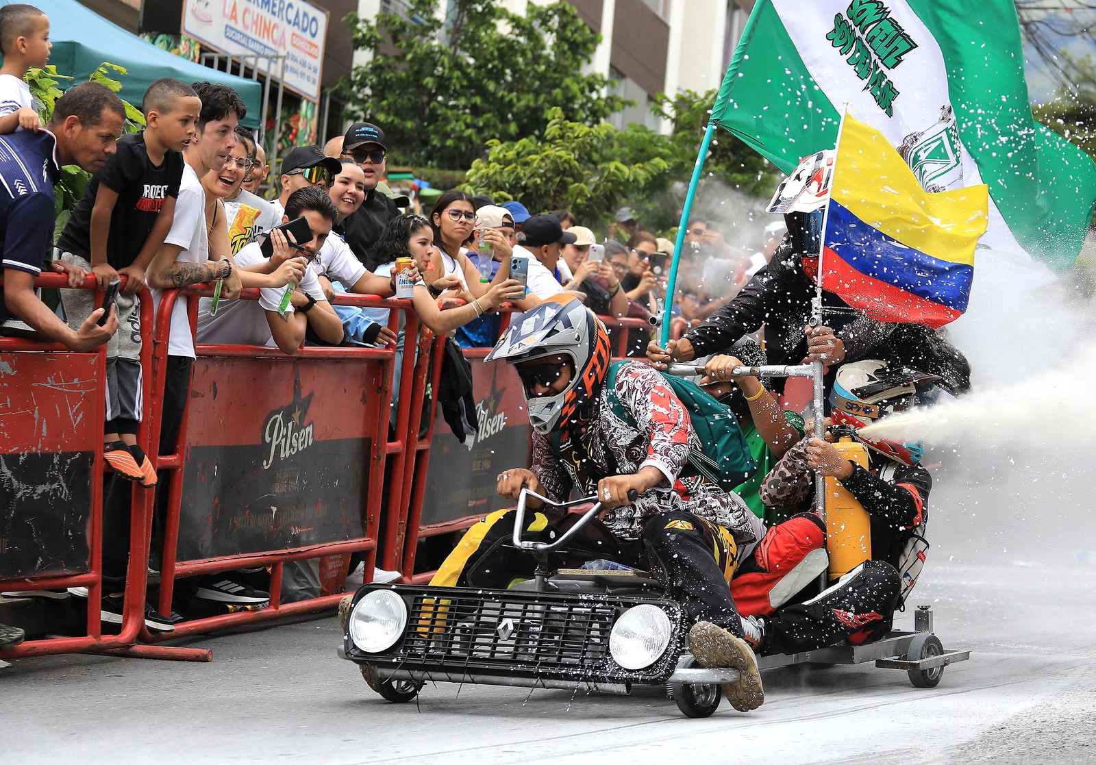 Several people ride on a cart past a crowd during a downhill race.