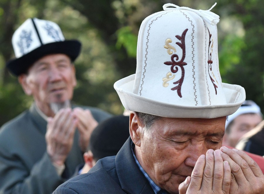 Several men wearing a traditional hat pray.