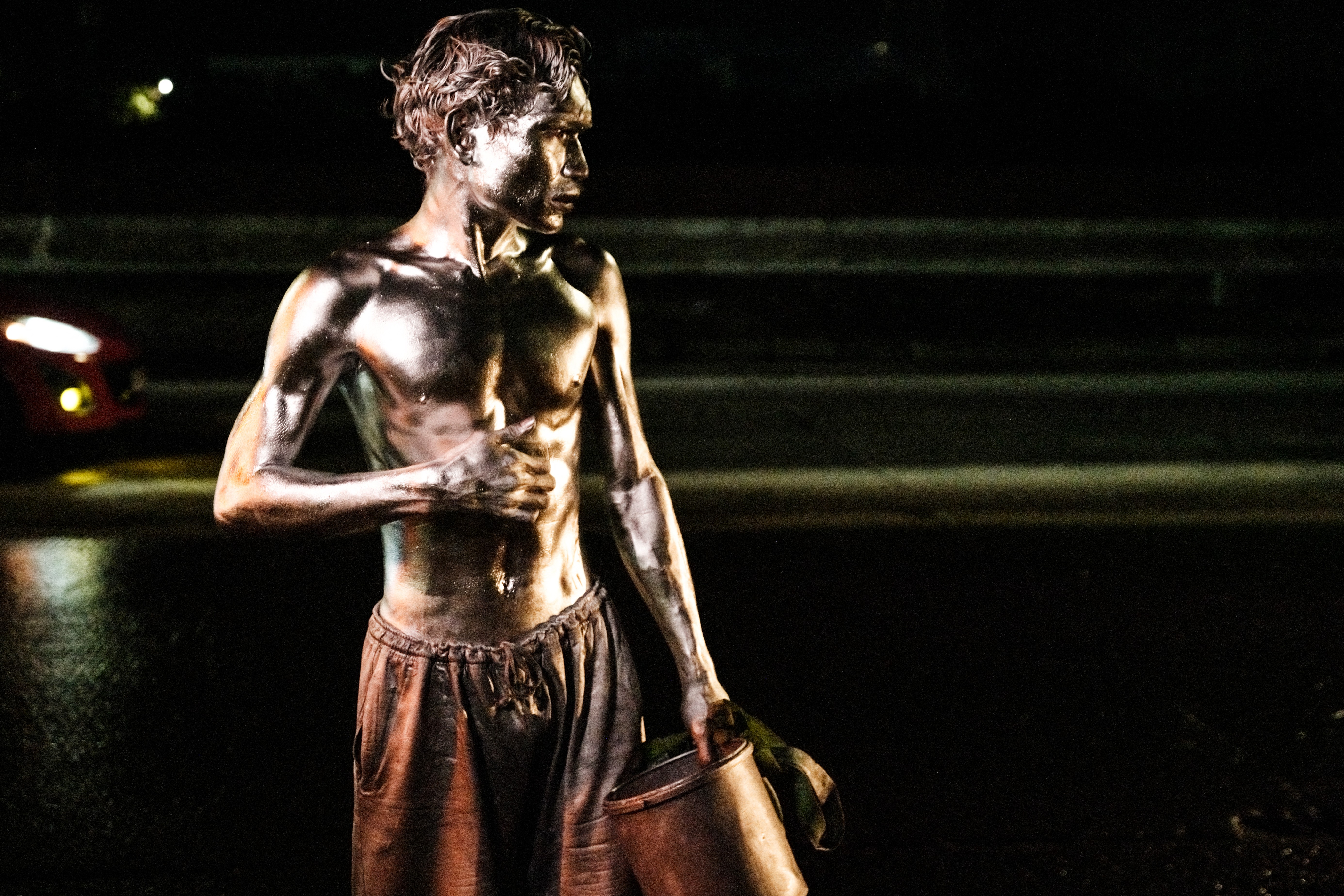 A close view of a shirtless street performer covered in silver paint