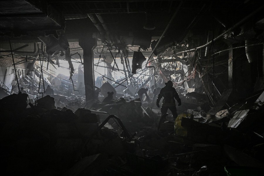 Emergency workers walk through debris inside a dark, destroyed shopping mall.