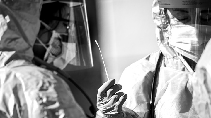 A black and white photo of two health care professionals in medical protective gear holding a cotton swab.