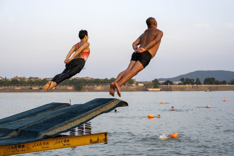 Two people leap from a springy diving board into a river.