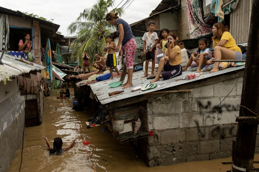 Women and children sit on rooftops, avoiding floodwater below.