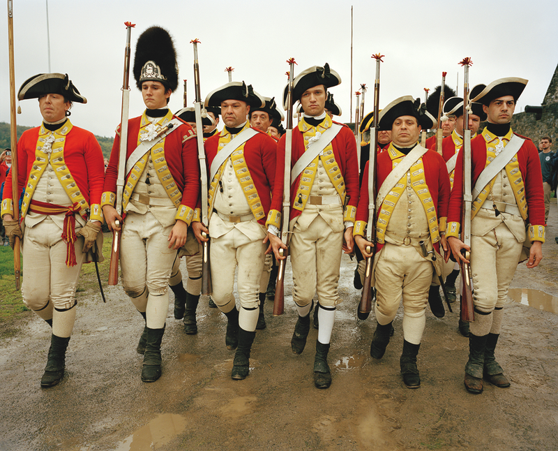 photo of reenactors as a troop of English soldiers marching together in formation to prepare for a musket demonstration