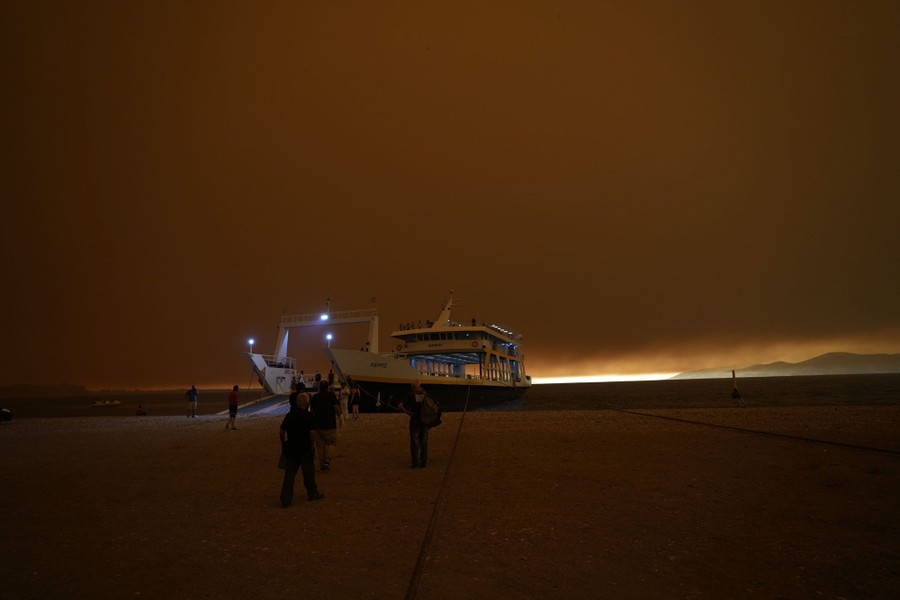 Dark smoke covers the sky above a ferry docked on a beach.