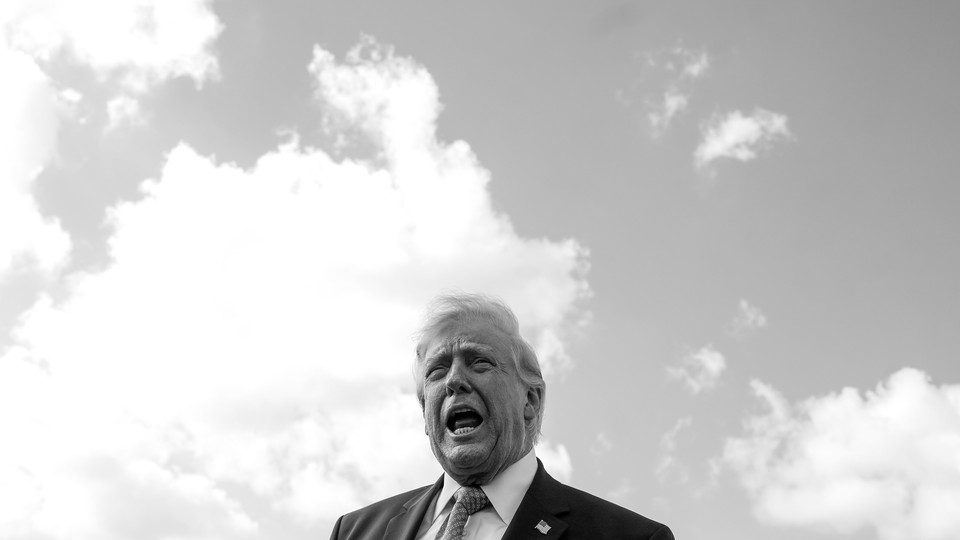 A black-and-white photograph of Donald Trump speaking from a low vantage point with the sky behind him