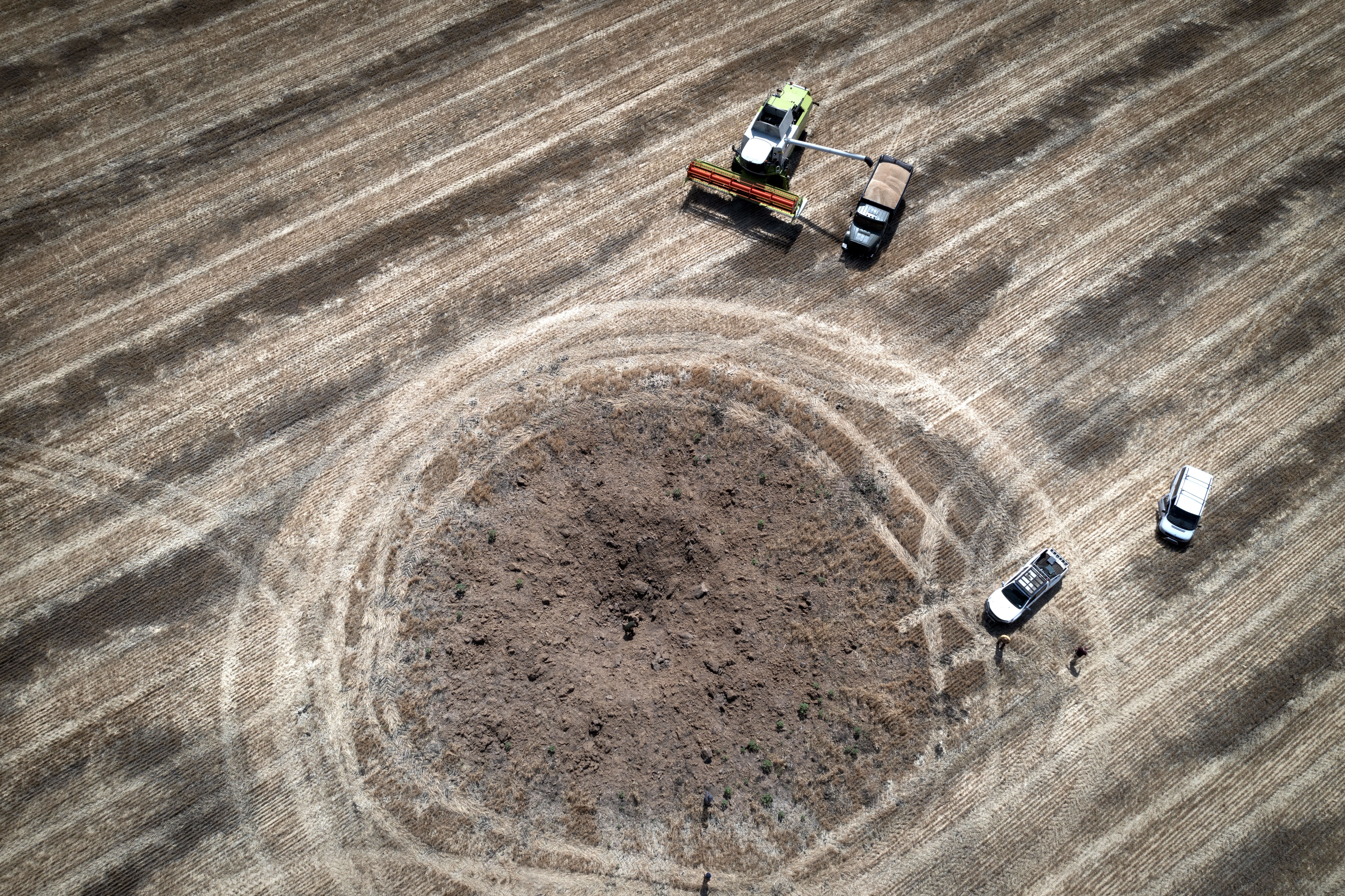 An aerial view of farm vehicles in a field near a fresh crater left by a Russian rocket.