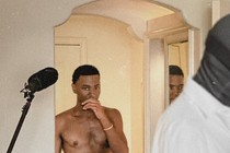 Jerrod Carmichael stands in front of a mirror next to a microphone.