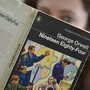 A woman, who's blurred out, holds a copy of George Orwell's '1984'