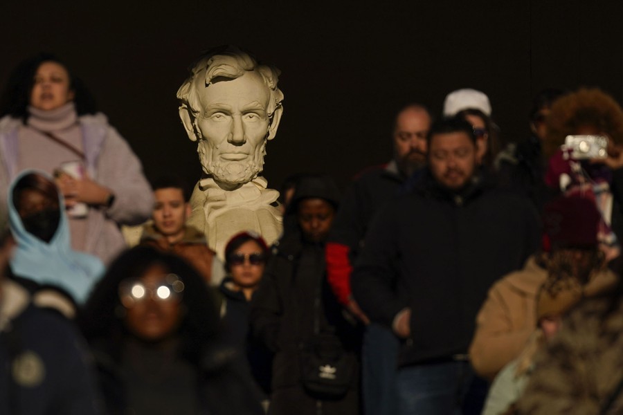 A crowd of people gather in front a large statue of Abraham Lincoln.