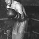 A black and white photographer of a boxer inside the corner of a ring with his left fist up