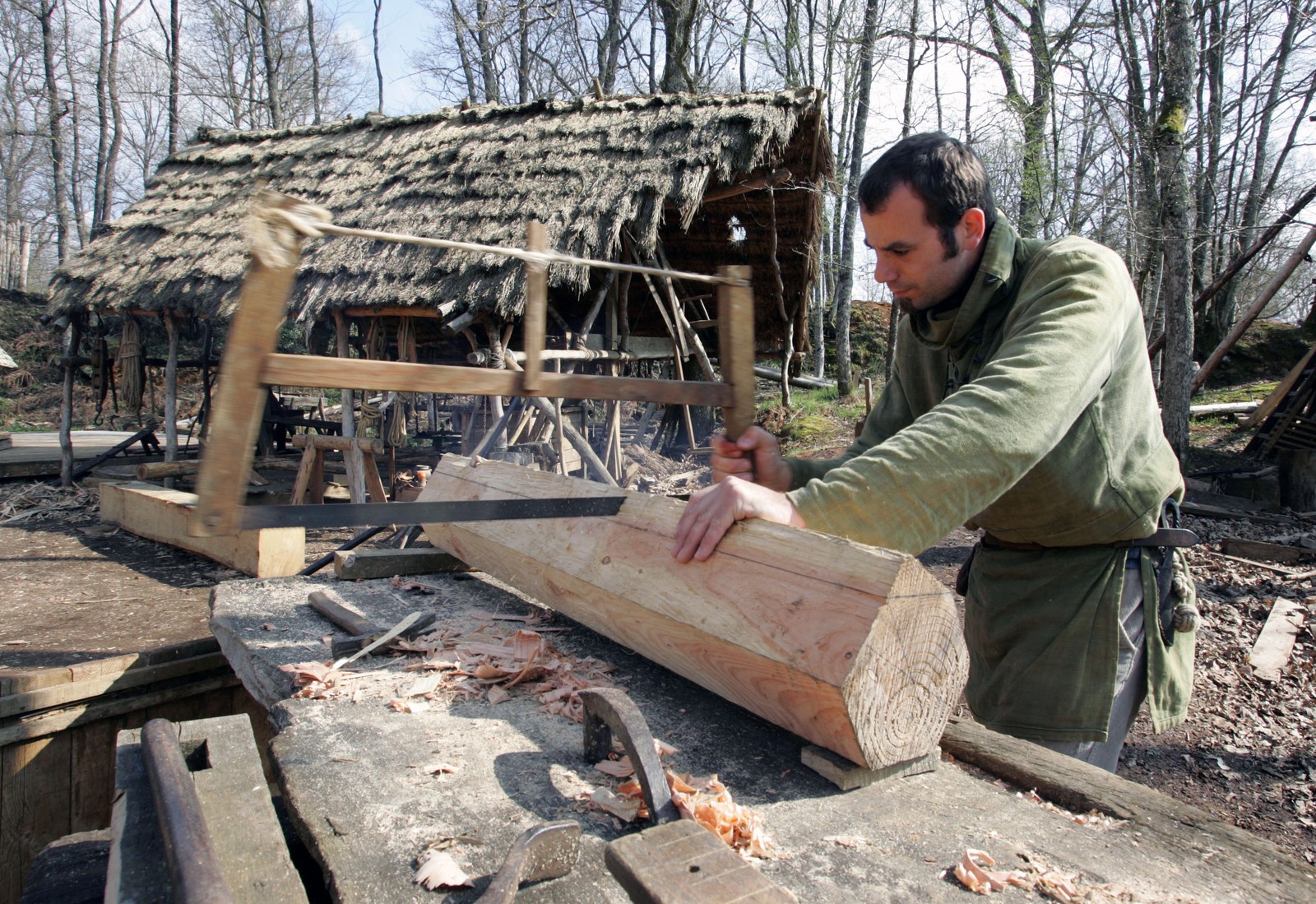 A carpenter uses an old hand-saw to cut into a thick piece of lumber at a construction site.
