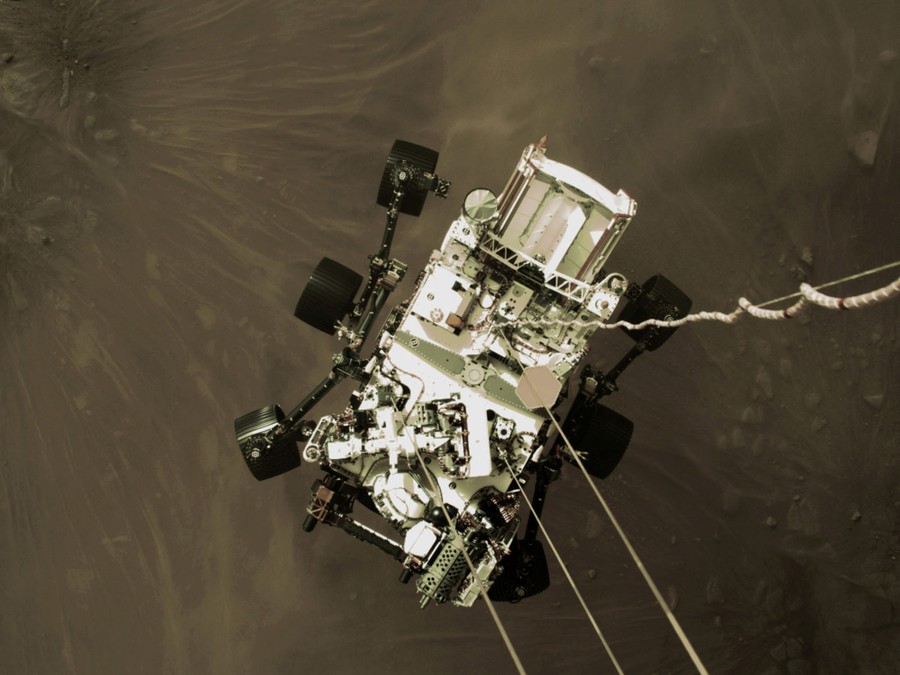 Looking down on the Mars rover, as it hangs from wires just above the surface of Mars
