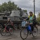 Balakliia residents riding bikes in front of a tank