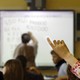 A student raises her hand as her teacher leads a lesson on a SmartBoard. Questions are being raised about whether teachers should be paid for the lessons they create.