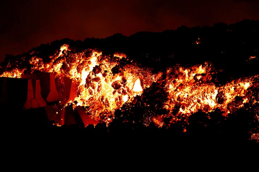 A thick lava flow pushes against a pile of concrete barriers, seen at night.