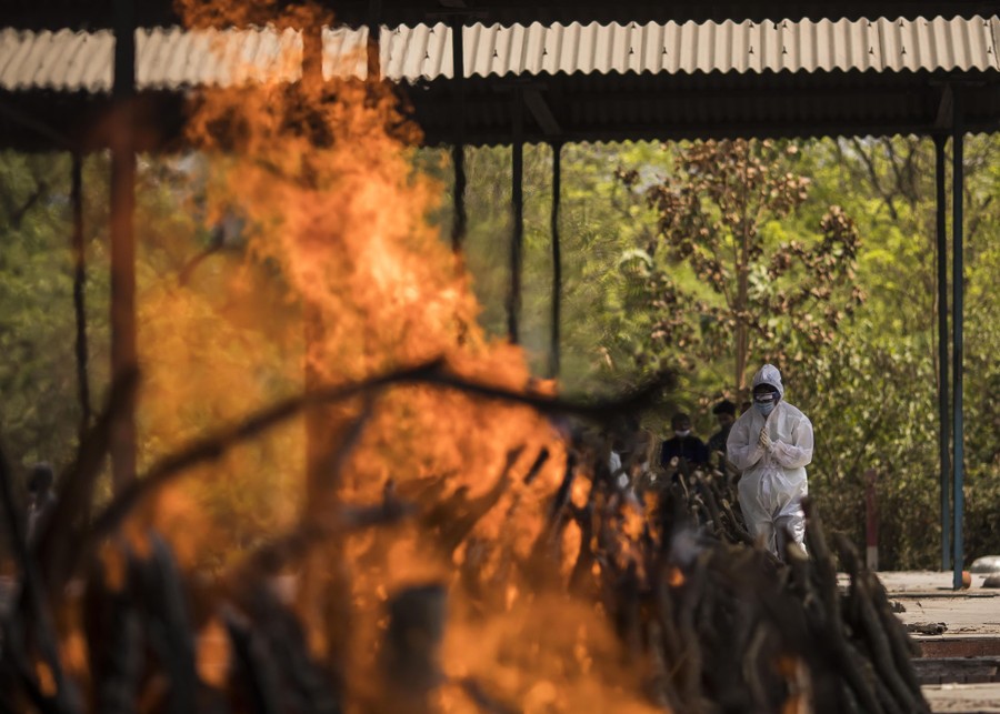 A man wearing protective gear prays near a burning funeral pyre.