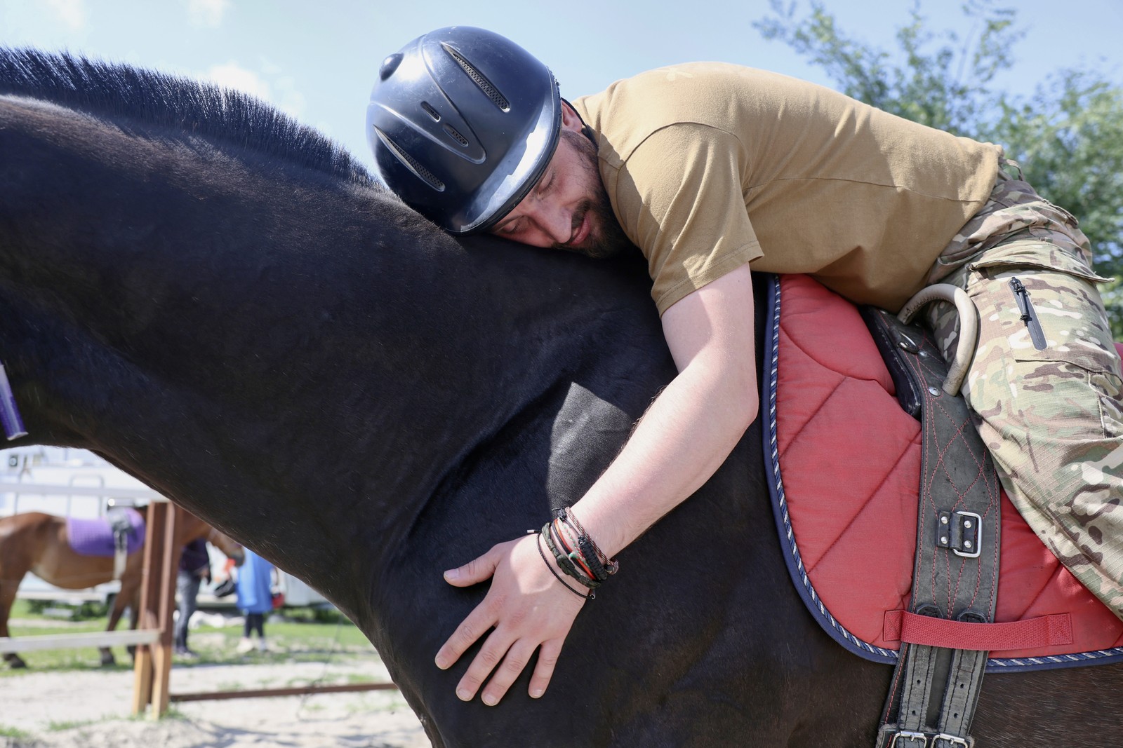 A soldier seated on a horse leans over and hugs the horse.