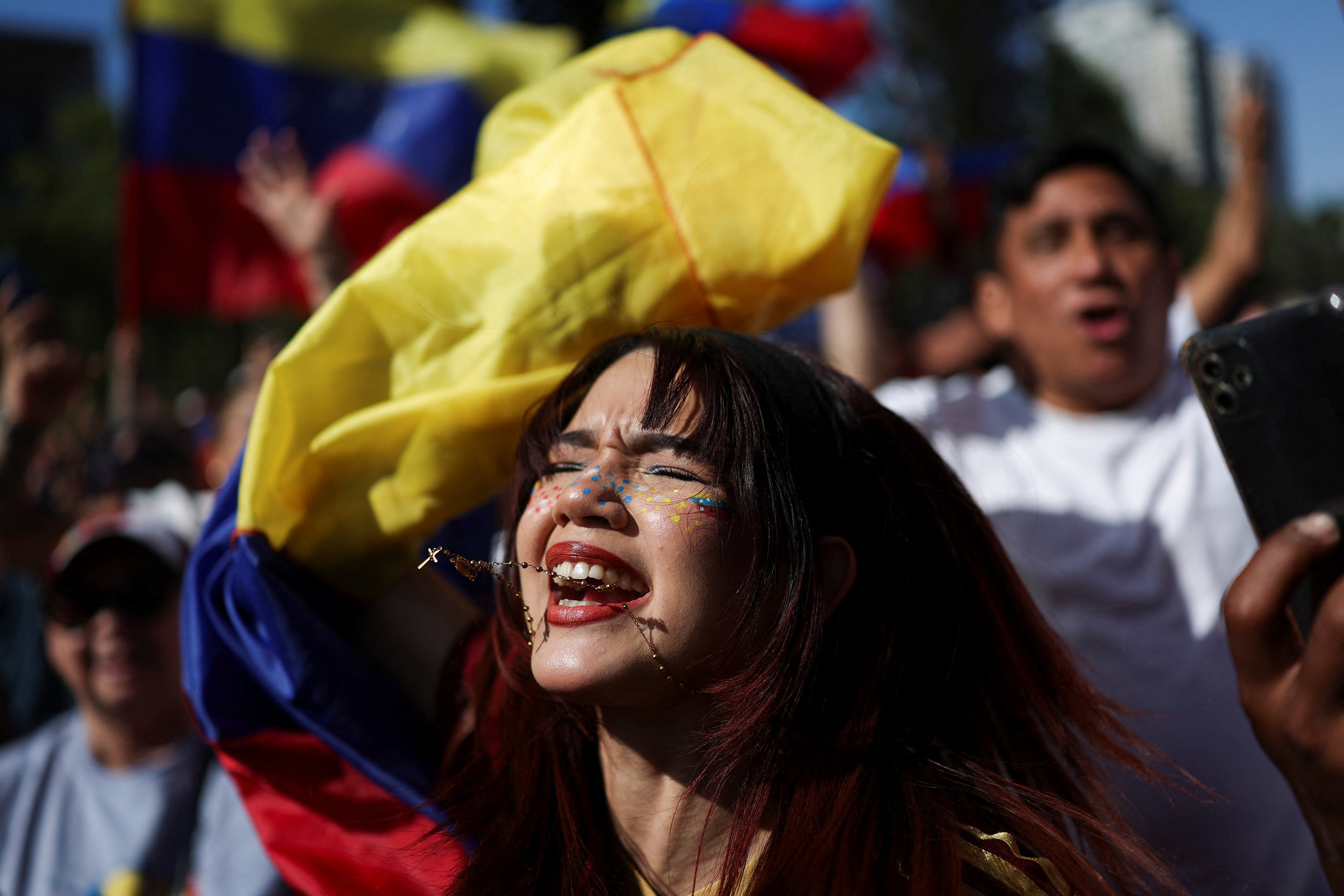 A woman reacts with joy while standing among others cheering and holding Venezuelan flags.