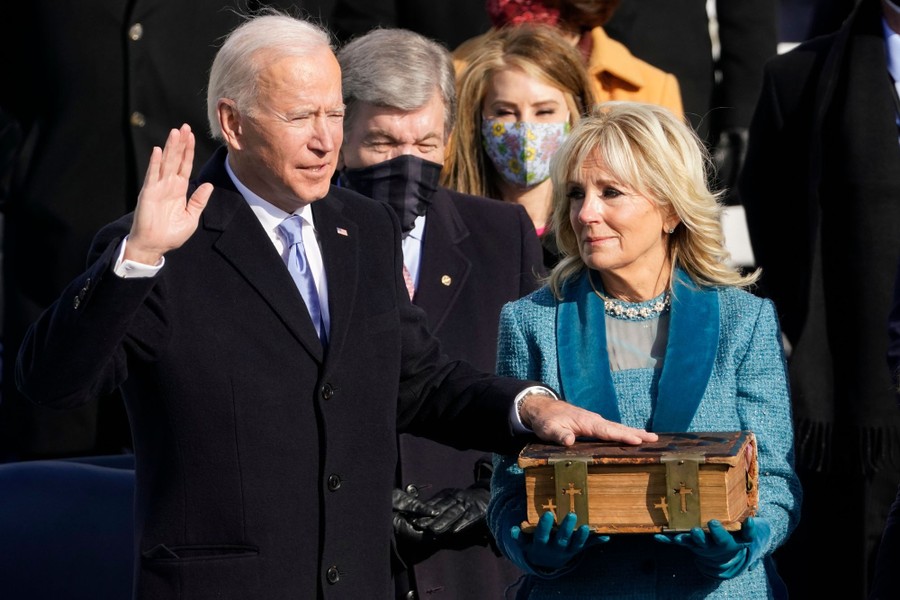 Joe Biden holds up his right hand, with his left hand on a large bible, held by his wife, Dr. Jill Biden.