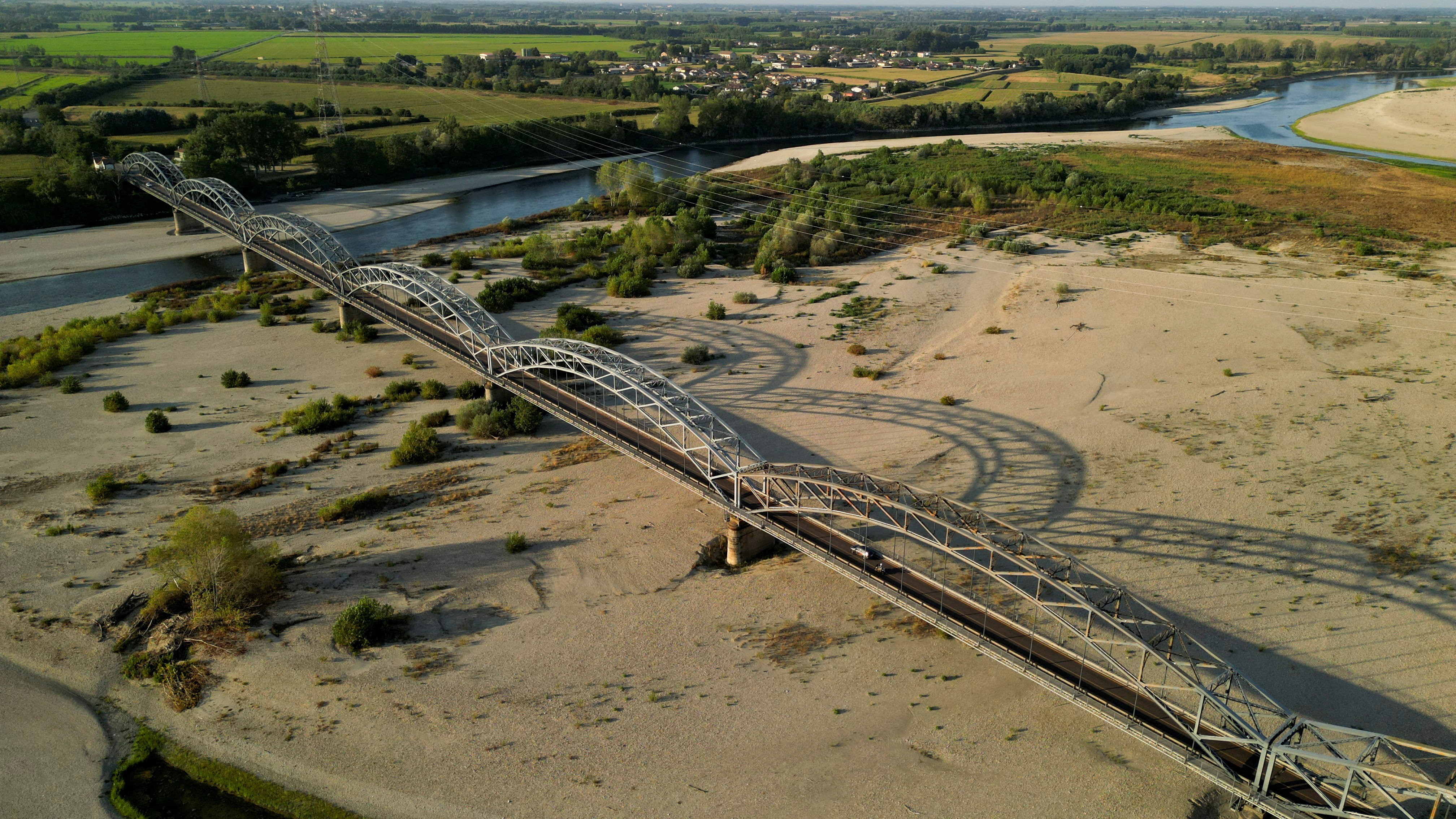 A drone view shows a river running low under a road bridge.