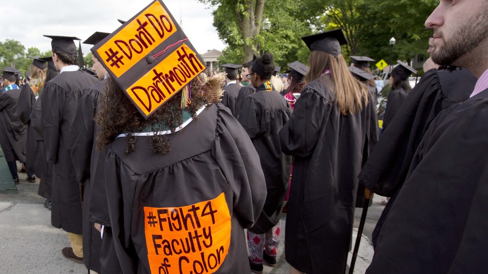 A student at graduation wears a cap that reads "Don't Do Dartmouth." The gown reads "Fight 4 Faculty of Color."