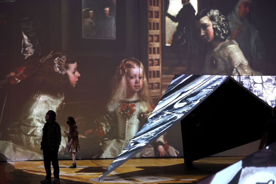 Several people look at artwork projected on several surfaces.