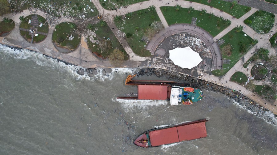 An aerial view of a cargo ship that was broken in two, stranded on a shoreline.