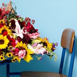 A profile view of a desk with flowers spilling off of it, against a blue background