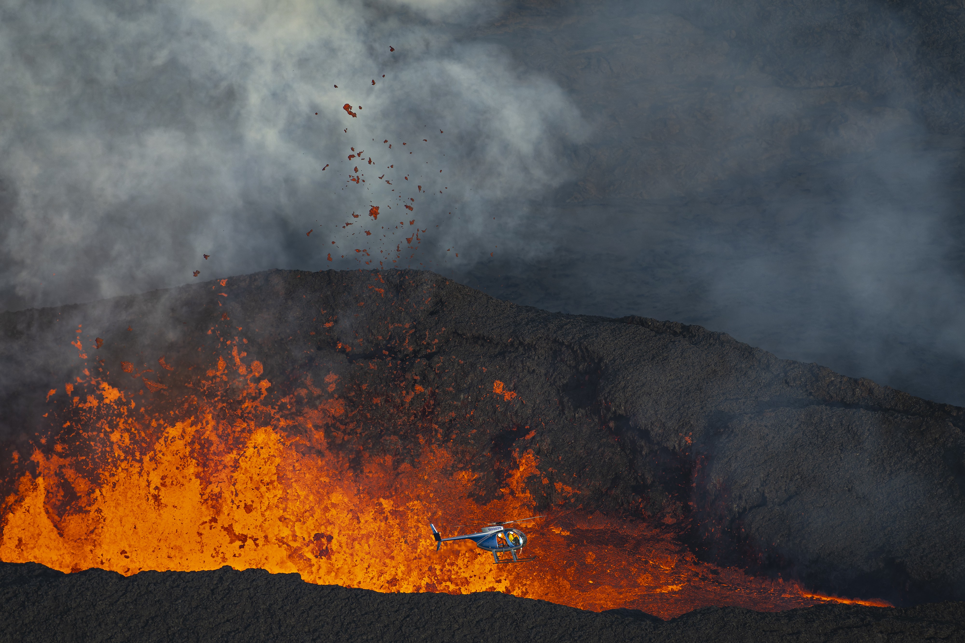 A helicopter flies low beside lava erupting from an active volcano.