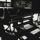 a black and white photo of two people sitting on a bench at a train station, from behind